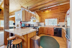 Eine Blockhausküche mit Holzsäulen, einer Mittelinsel, Barhocker, einem Geschirrspüler und einem großen Kühlschrank.