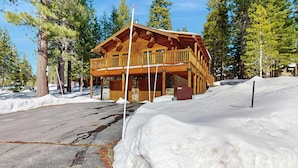 Een houten lodge met een balkon, omgeven door sneeuw en bomen.