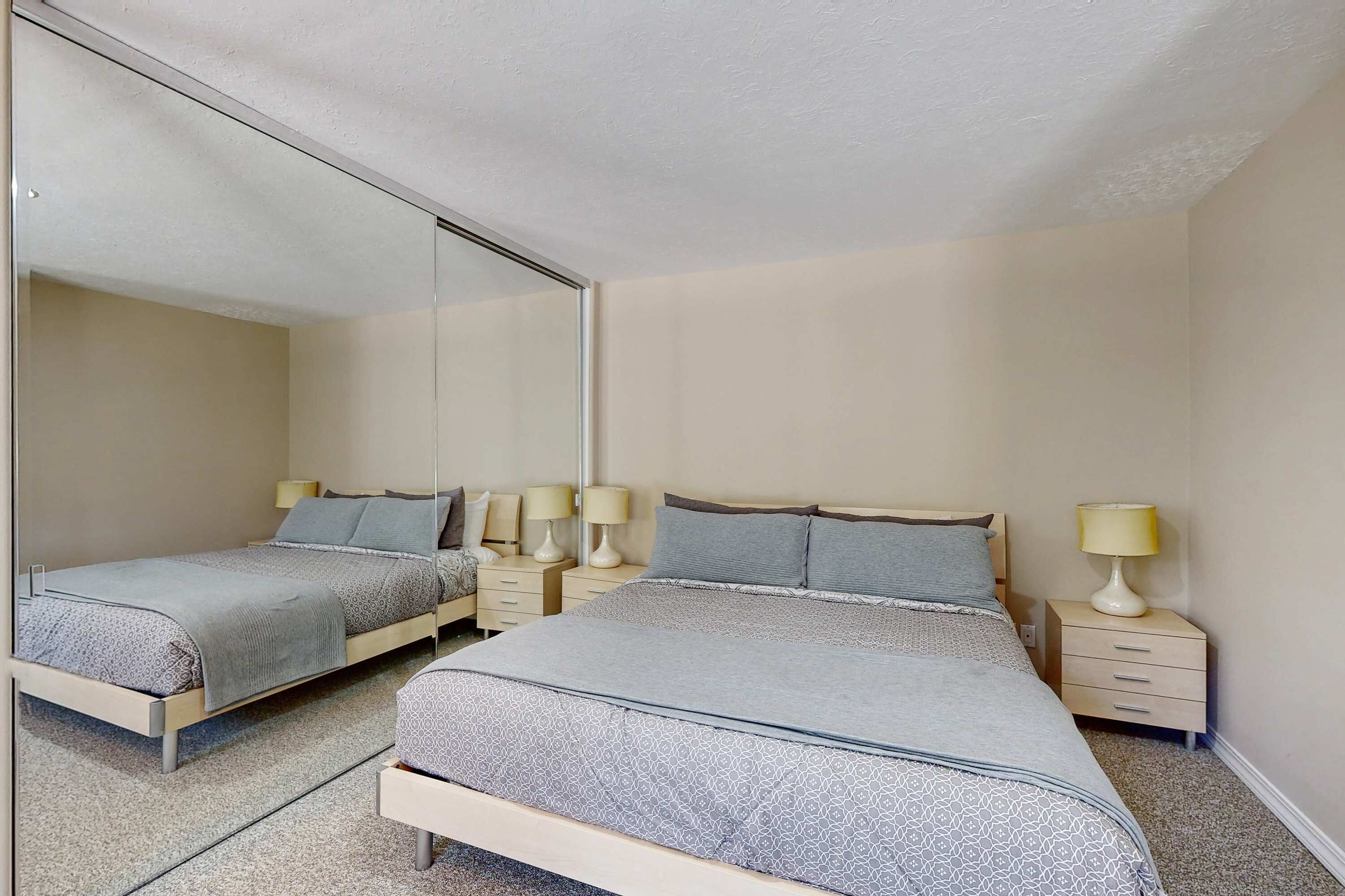 Un dormitorio con dos camas, mesitas de noche con lámparas y un espejo grande en la pared.