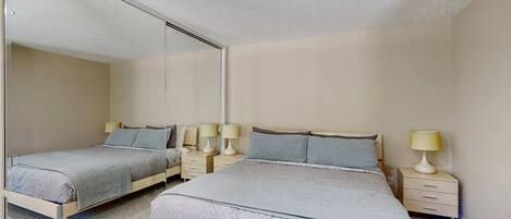 Un dormitorio con dos camas, mesitas de noche con lámparas y un espejo grande en la pared.