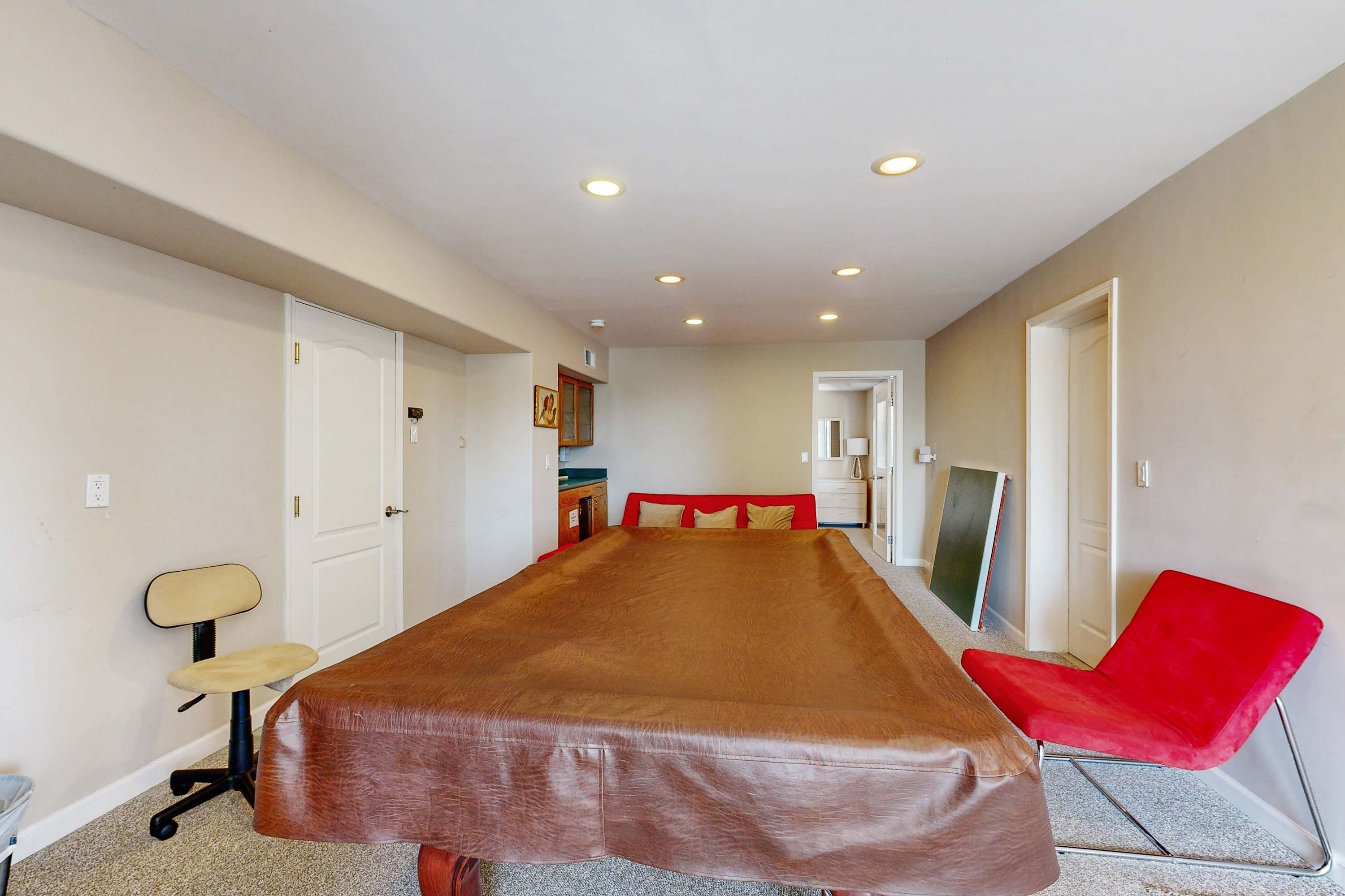 A room with a long table, a red chair, a desk, and a chair with a high backrest.