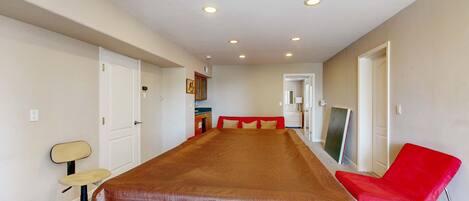 A room with a long table, a red chair, a desk, and a chair with a high backrest.