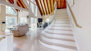 Ein großzügiger Wohnbereich mit einer geschwungenen Treppe, großen Fenstern und einer hohen Decke mit freiliegenden Balken.