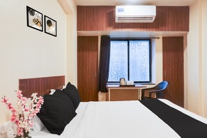 A hotel room with a bed, a desk, a chair, an air conditioner, and a window with curtains.