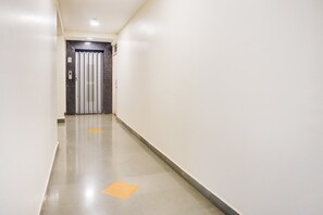 A hallway with a door at the end, a light switch, and a vent on the wall.