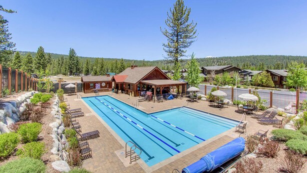 A pool area with lounge chairs, a wooden building, and a forested backdrop. - Quiet Townhouse in Ideal Truckee Location with Pool, Hot Tub & Sauna (Truckee)