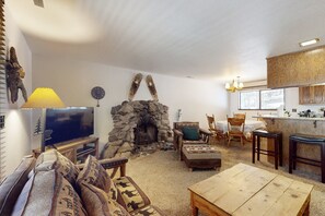 Ein gemütliches Wohnzimmer mit Kamin aus Stein, einem Fernseher und rustikalen Möbeln.