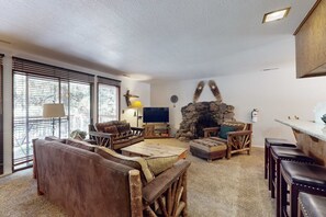 Ein Wohnzimmer mit Kamin aus Stein, einem Flachbildfernseher und einer Essecke mit Holzstühlen.
