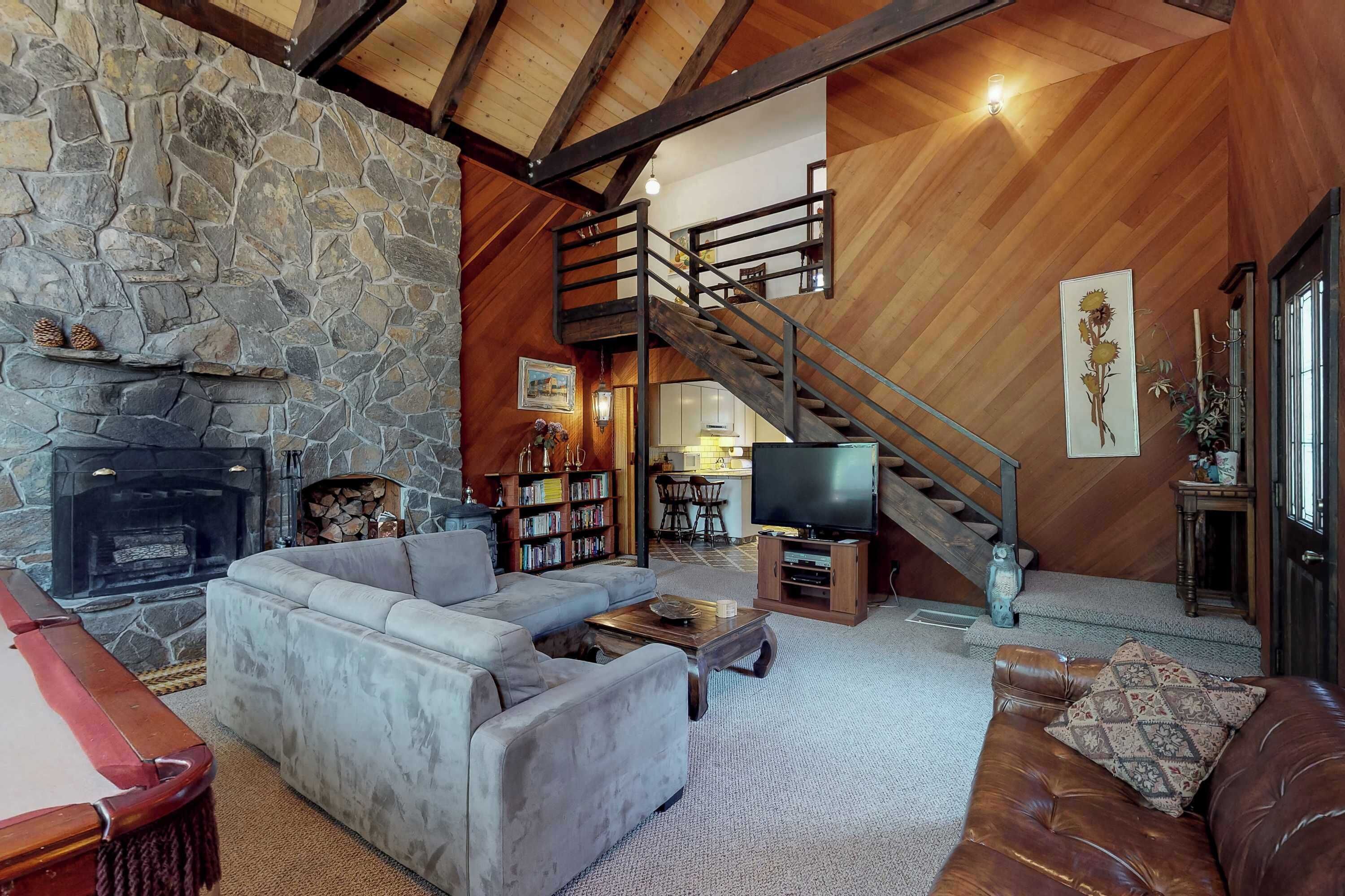 A cozy living room with a stone fireplace, a sofa, a pool table, a staircase, and a television.