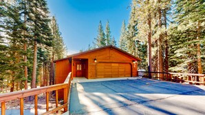 Een houten chalet met garage, omgeven door hoge bomen.