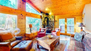 Een chaletinterieur met een stenen open haard, houten plafond en grote ramen.