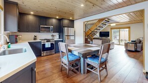 A modern kitchen with dark cabinets, stainless steel appliances, and a wooden dining table with chairs. - Remodeled Lake Tahoe Beach Condo - Pools, Tennis & Deck - Near Ski Resorts (Tahoe City)
