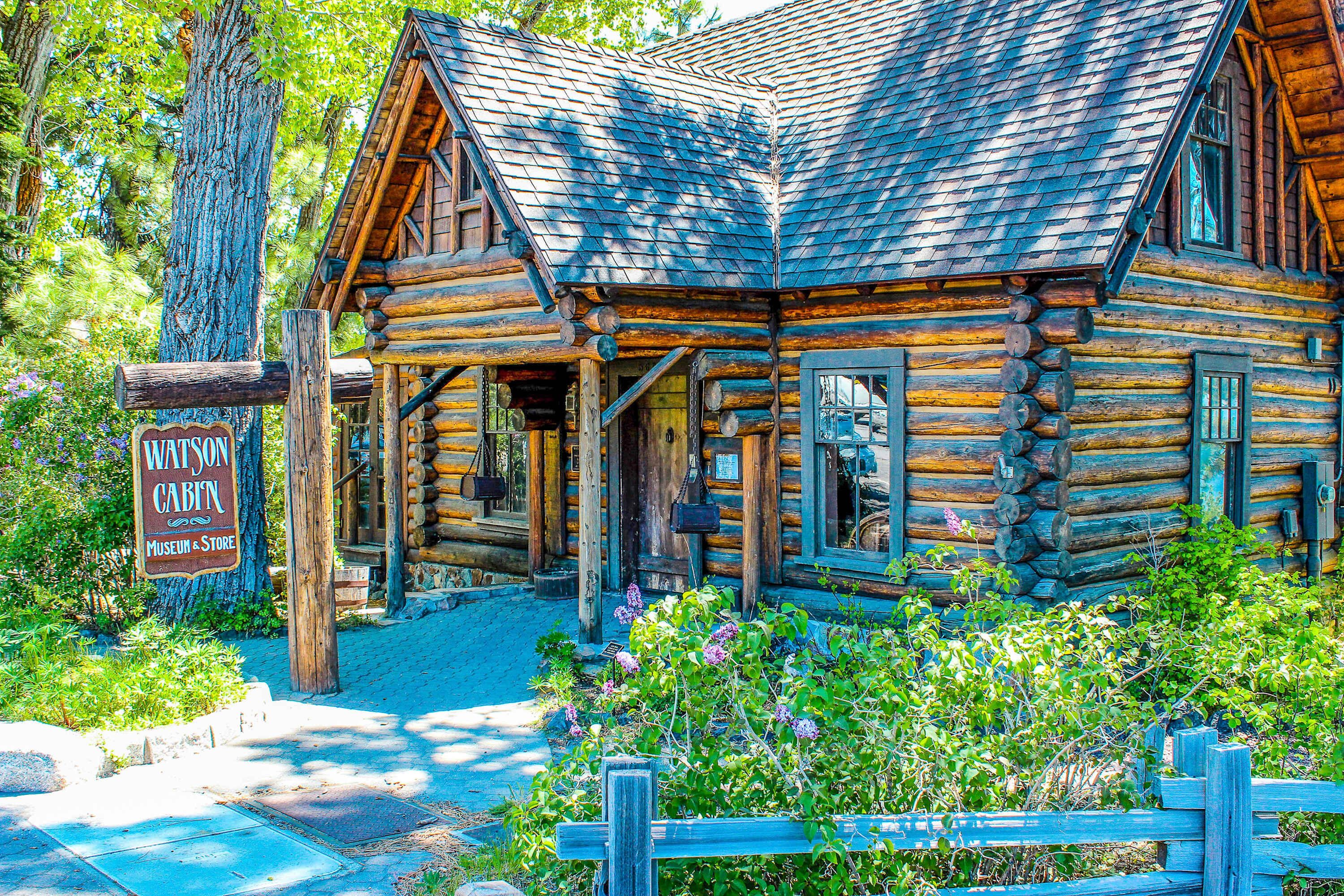Een blokhut met veranda, een bord waarop staat 'Watson Cabin Museum & Store', en een houten hek voor de hut.