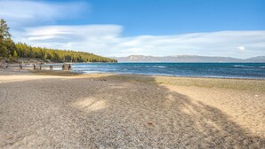 A beach with a wooden bench, a trash bin, and a forested area in the background. - Remodeled Lake Tahoe Beach Condo - Pools, Tennis & Deck - Near Ski Resorts (Tahoe City)