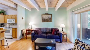 A living room with a couch, coffee table, and a view through a large window. - Forest-view condo with wood fireplace & walkable locale - dog-friendly (Incline Village)