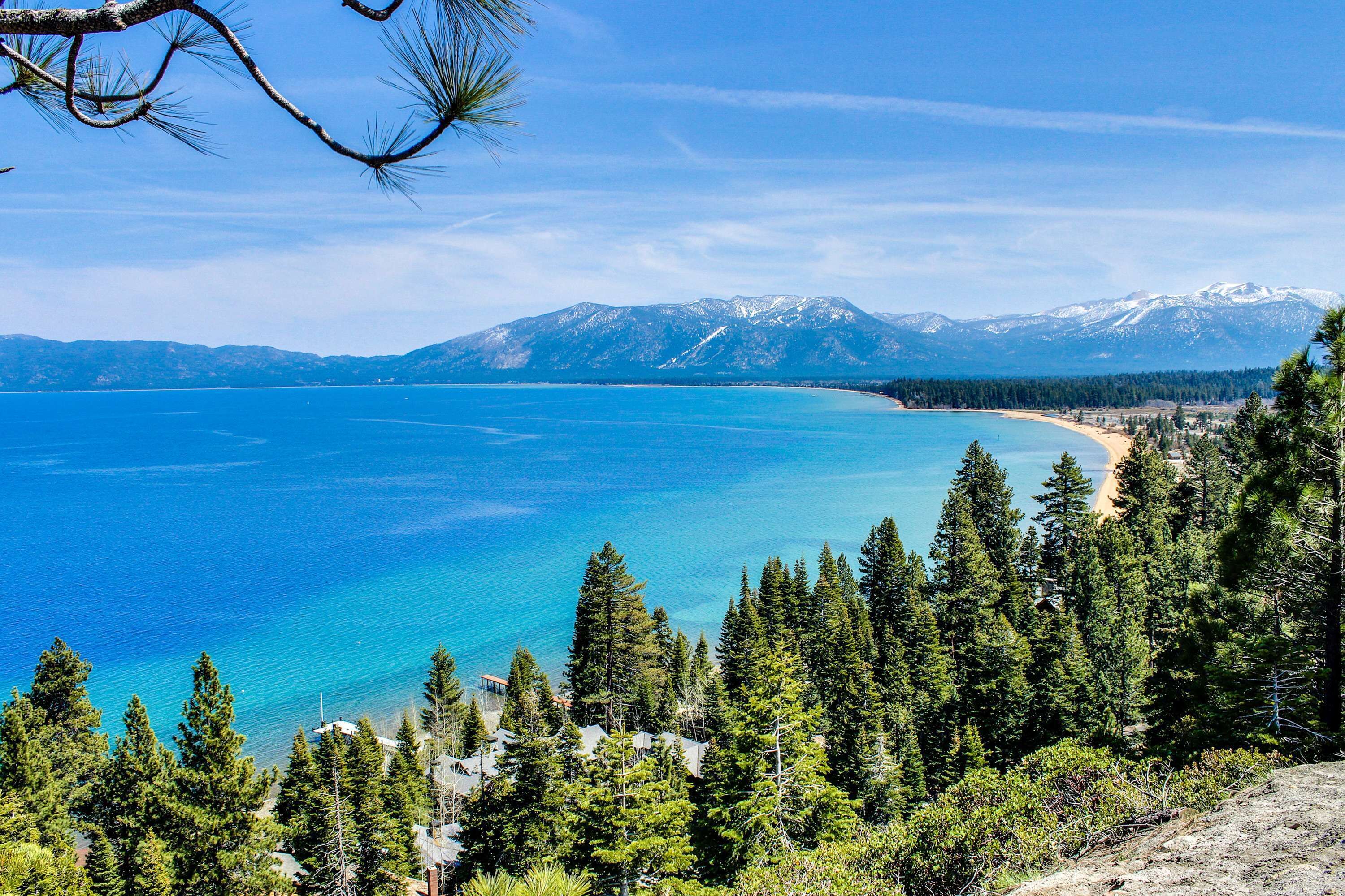A coastal landscape with a clear view of a mountain range, dense forest, and a beach.