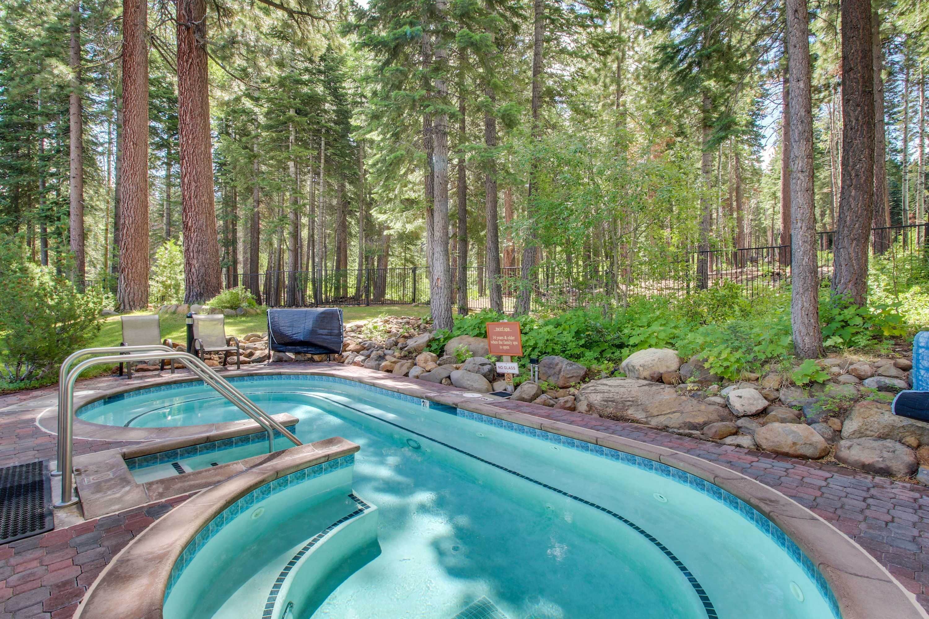 A swimming pool with a stone border, surrounded by a forest.