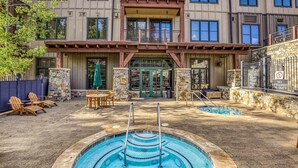 Zona de piscina con hidromasaje, sillas de descanso y una pared de piedra.