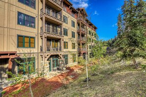 Un edificio de varios pisos con balcones, fachada de piedra y zona boscosa circundante.