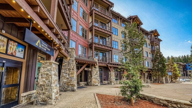 Un edificio de varios pisos con pilares de piedra, un letrero que dice Tahoe Mountain Club, y un camino pavimentado.