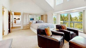 Ein geräumiges Schlafzimmer mit einem großen Bett, einer Sitzecke mit Ledersesseln und einem Balkon mit Blick auf Bäume.