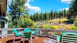 Eine Holzterrasse mit Gartenmöbeln, einem Geländer und Blick auf einen bewaldeten Hang.