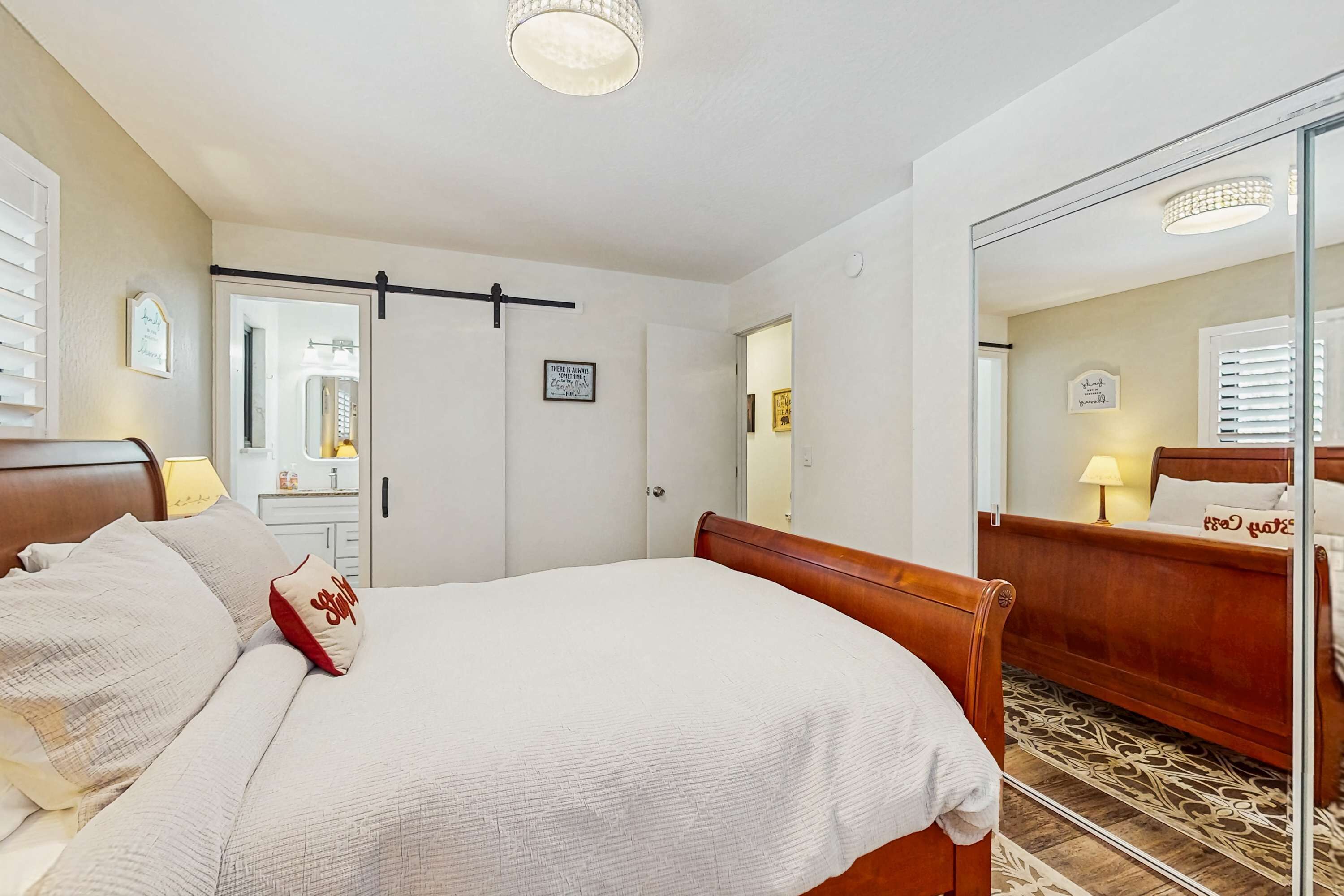 A bedroom with a bed, a bedside table, a mirror, and a door.