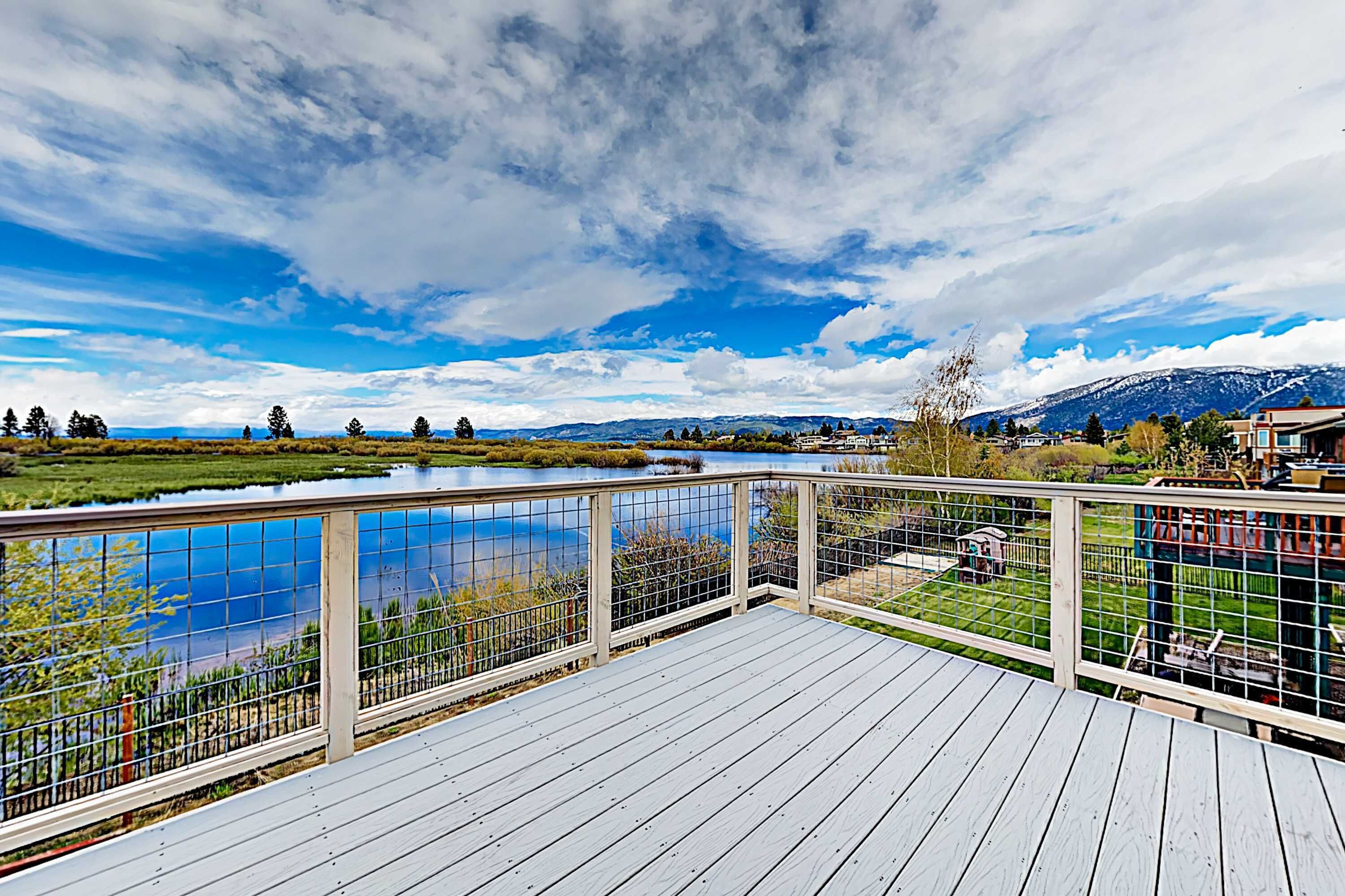 A deck with a view of a river, mountains, and a clear sky.