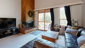 A living room with a television, fireplace, sofa, and a view through large windows. - Mountain Condo with Fireplace, Balcony, WiFi (NorthStar-Truckee)