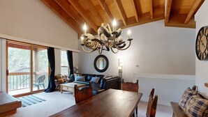 A spacious living area with a wooden ceiling, a chandelier, a dining table, and a large clock on the wall. - Mountain Condo with Fireplace, Balcony, WiFi (NorthStar-Truckee)