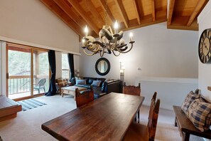 A spacious living area with a wooden ceiling, a chandelier, a dining table, and a large clock on the wall. - Mountain Condo with Fireplace, Balcony, WiFi (NorthStar-Truckee)
