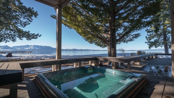 Een hottub met uitzicht op een meer en bergen, omringd door een houten terras en banken.