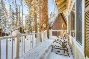 Une cabane en bois avec un porche enneigé, une clôture en bois et un grand arbre en arrière-plan.