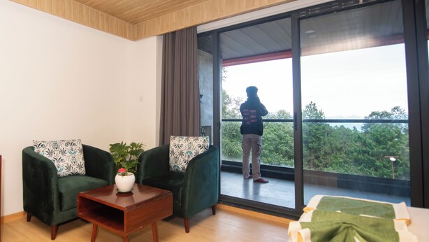 Ein modernes Zimmer mit zwei grünen Sesseln, einem Holztisch und Blick auf Grün hinter einer großen Schiebetür.