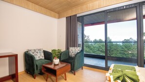 Ein Zimmer mit zwei grünen Sesseln, einem Holztisch, einem weißen Sofa und einem großen Fenster mit Blick auf Bäume.