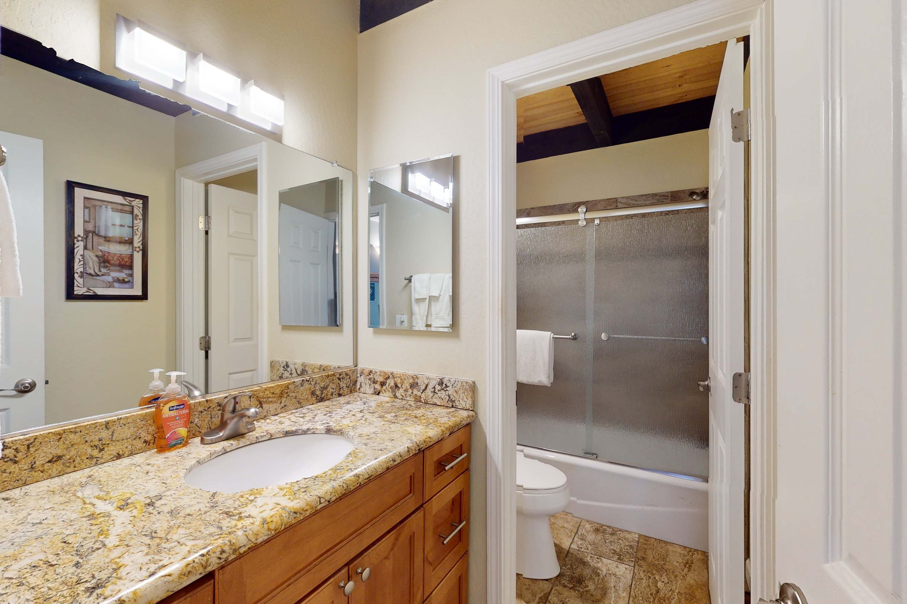 A bathroom with a granite countertop, white sink, and a glass shower enclosure.
