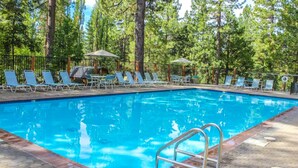 A swimming pool with lounge chairs and umbrellas, surrounded by trees. - Beautiful Condo with Shared Pool & Tennis Courts, Close to Northstar (Kings Beach)