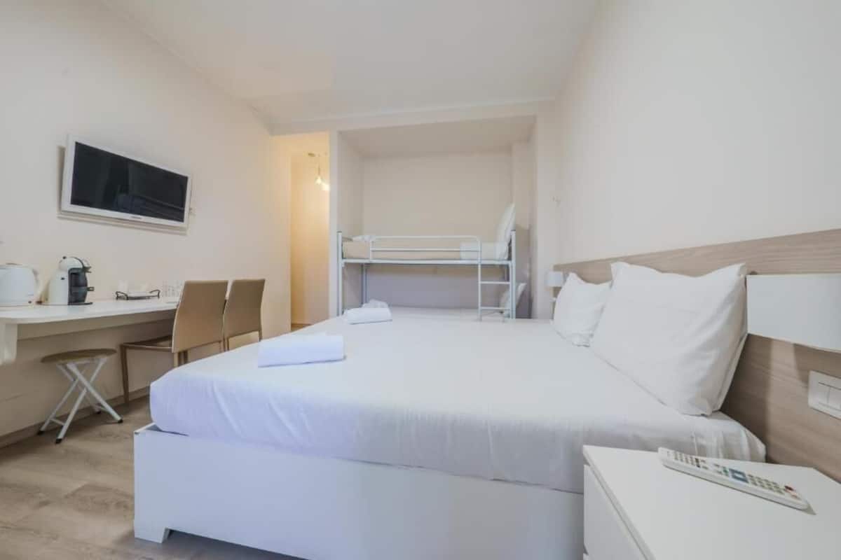 A hotel room with a bed, a desk, a chair, a TV, and a bedside table.