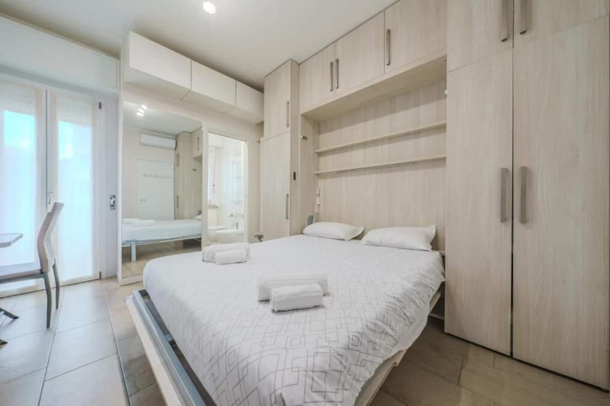 A modern bedroom with a large bed, built-in wardrobe, and a bathroom visible through an open door.