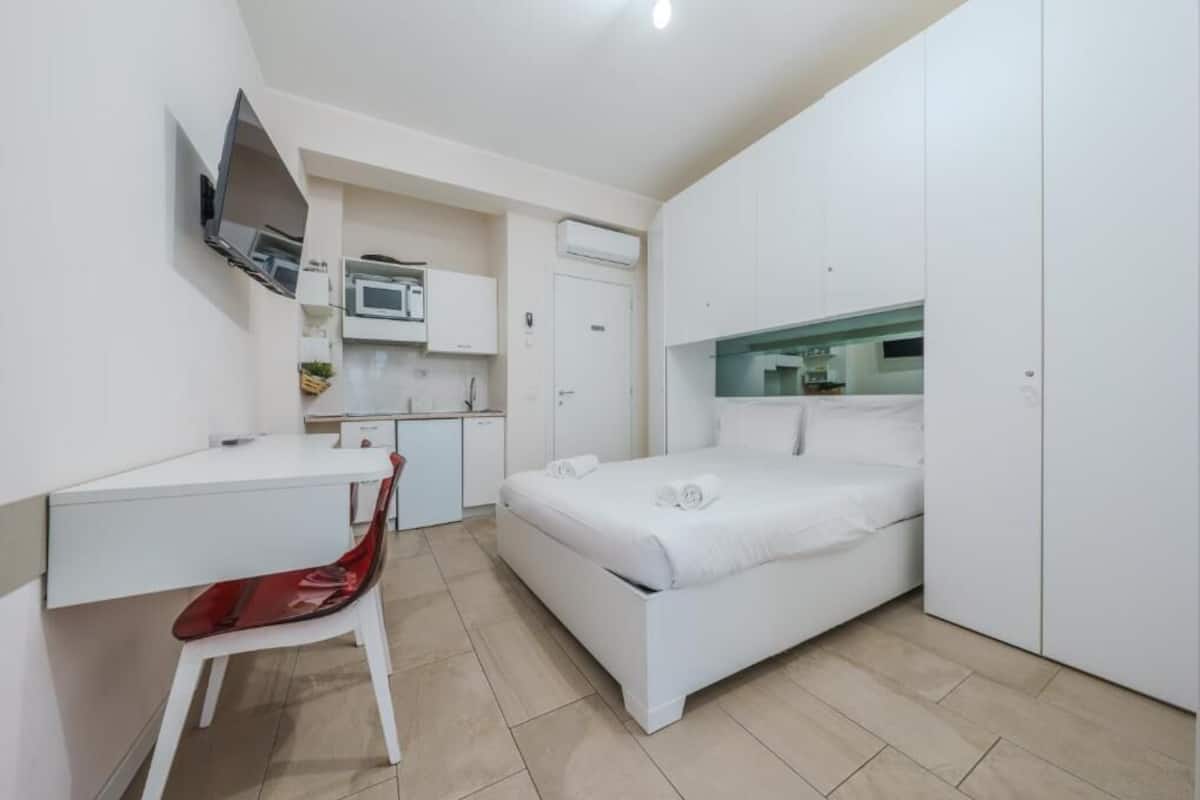 A compact room with a bed, a desk, a chair, a TV, a microwave, and a wardrobe.