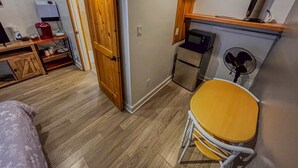 Une pièce de taille modeste avec une porte en bois, une petite kitchenette, un four à micro-ondes, un ventilateur et une table jaune.