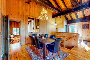 Ein Holzinterieur mit einem Esstisch, Stühlen, einer Chandelier und einem gemusterten Teppich.