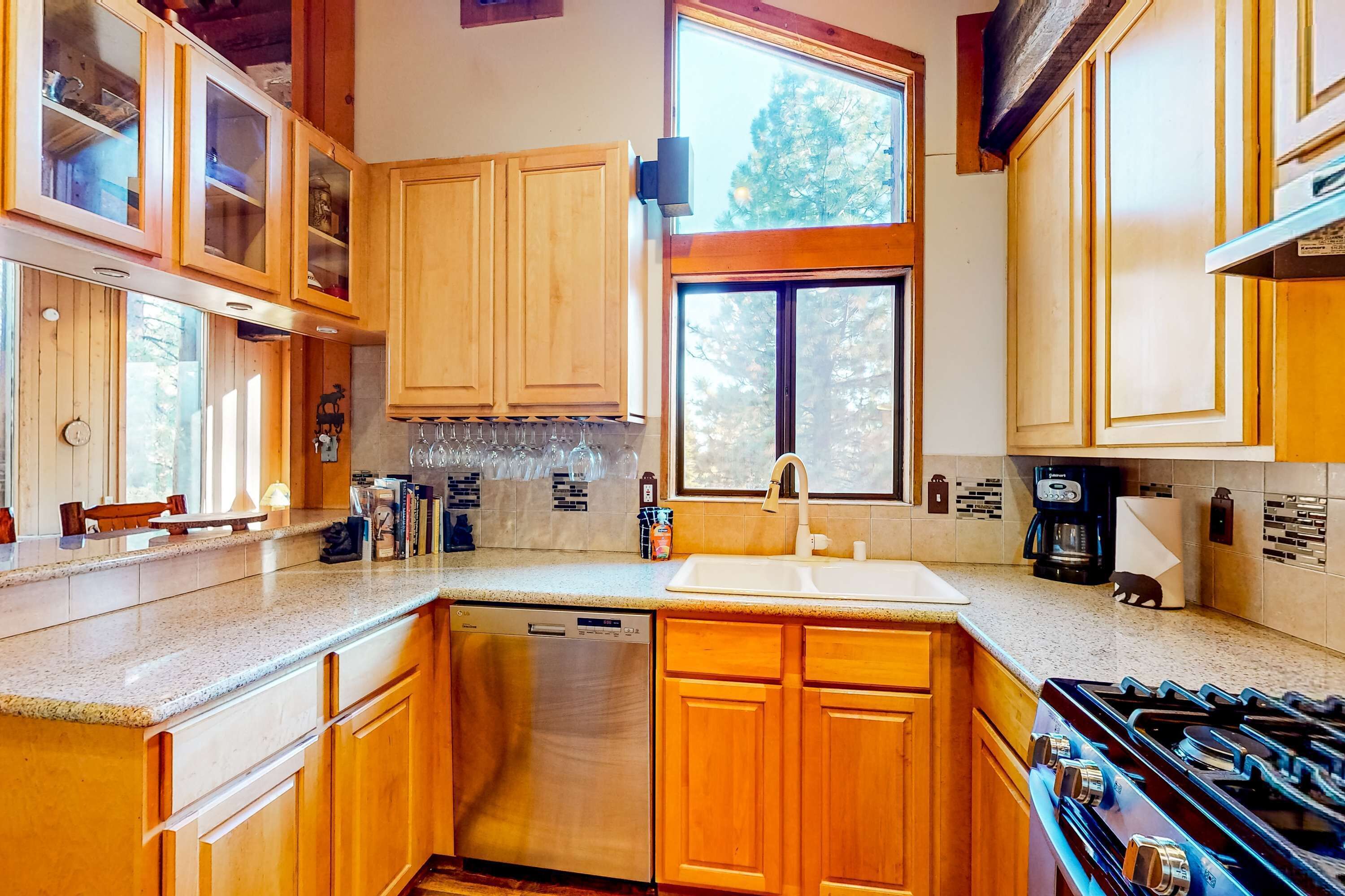 A kitchen with wooden cabinets, a dishwasher, a stove, and a window with a view of trees.