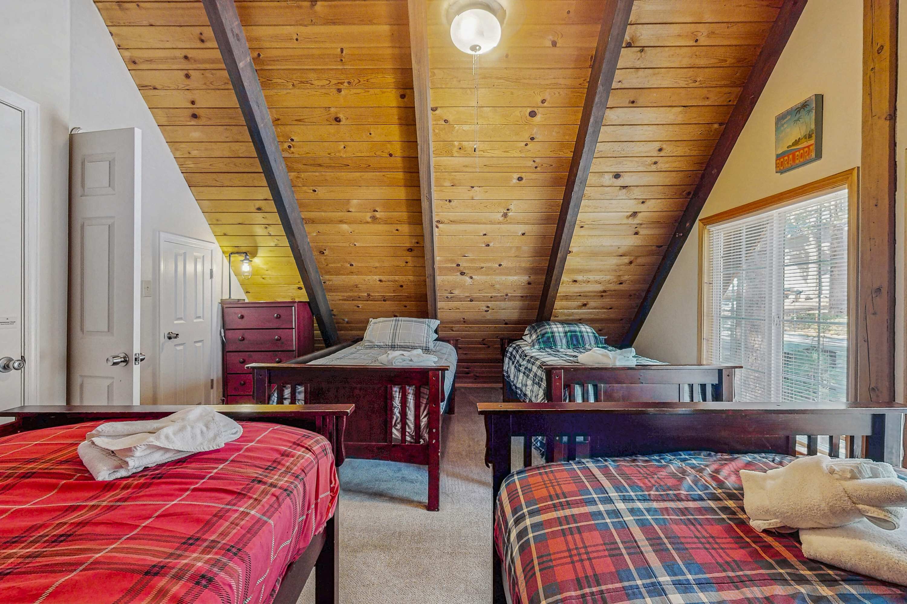 A room with wooden beams, two beds with plaid bedding, a dresser, and a window with blinds.