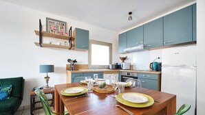 A modern kitchen with teal cabinets, a dining table set with plates and glasses, and a green sofa in the living area. - Balcony facing Pontaillac beach, garage, sleeps 4. (Royan)