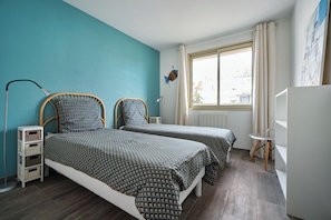 A bedroom with two beds, a window, a radiator, and a desk.