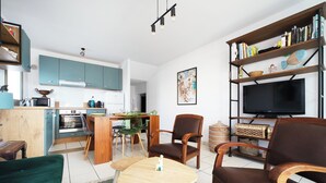 A modern kitchen with teal cabinets, a dining area with a wooden table and chairs, a living room with a TV and bookshelves, and a green sofa. - Balcony facing Pontaillac beach, garage, sleeps 4. (Royan)