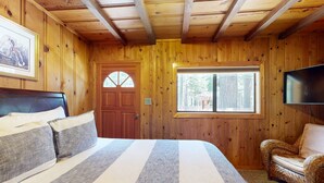 Ein Zimmer mit Holzwänden, einem Bett, einem Korbstuhl, einem Fernseher und einem Fenster.