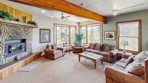 A living room with a stone fireplace, wooden ceiling beams, large windows, and a fireplace mantel. - Lake- & mountain-view lodge with hot tub, rooftop deck & pool table, sleeps 10 (Zephyr Cove)