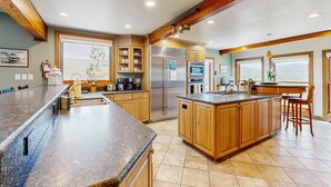A modern kitchen with granite countertops, wooden cabinets, stainless steel appliances, and large windows offering a view. - Lake- & mountain-view lodge with hot tub, rooftop deck & pool table, sleeps 10 (Zephyr Cove)